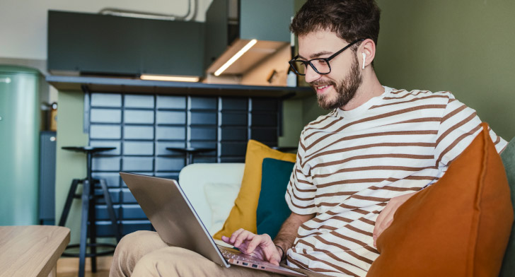 Personne assise sur un canapé utilisant un ordinateur portable pour préparer l’achat d’un premier bien immobilier