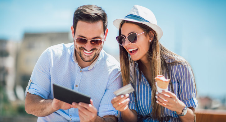 Deux jeunes adultes utilisant une tablette et une carte bancaire en terrasse.