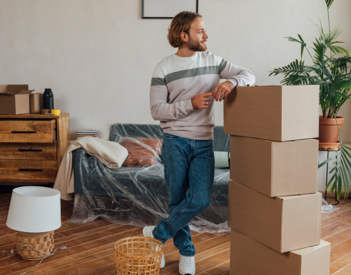 Jeune adulte entouré de cartons dans son nouveau logement, prêt à s’installer